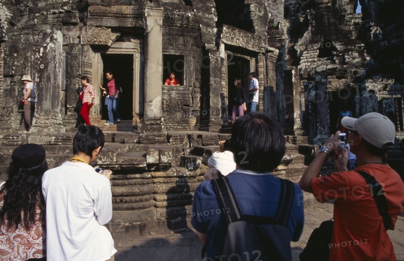 CAMBODIA, Siem Reap Province, Angkor Thom, The Bayon.  Tourists posing for photographs amongst the temple architecture.