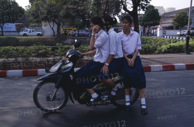THAILAND, North, Chiang Mai, Speeding moped carrying three girls dressed in uniform with the driver talking on a mobile phone.