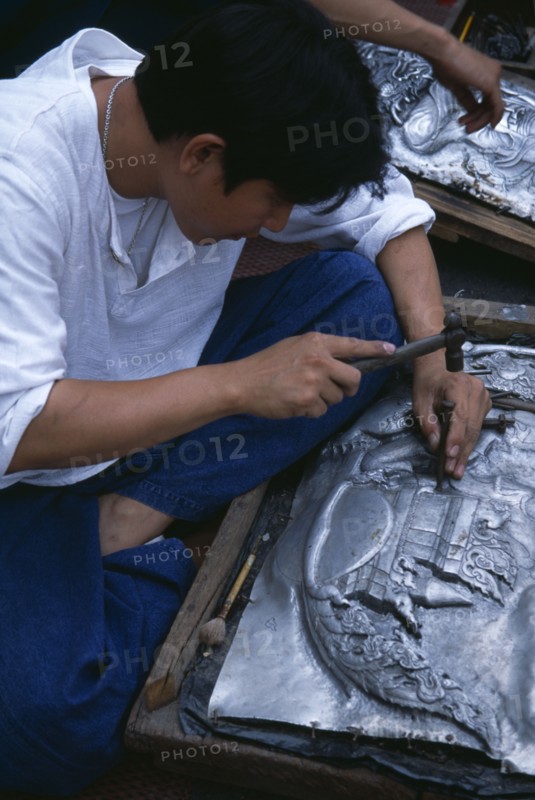 THAILAND, North, Chiang Mai , Tha Phae Road.  Young man working on metal work relief picture.