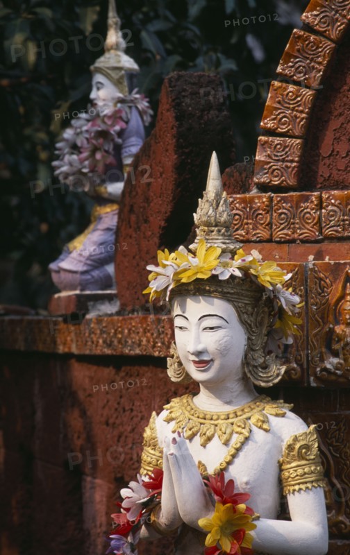 THAILAND, North, Chiang Mai, Wat Bupparam Temple on Tha Phae Road. Detail of brightly coloured Buddha statues decorated with floral garlands.