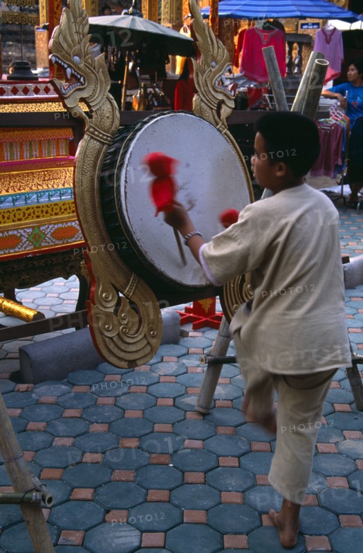 THAILAND, North, Chiang Mai, Wat Chettawan on Tha Phae Road.  Young boy playing drum suspended on frame with red and gold dragon carvings.