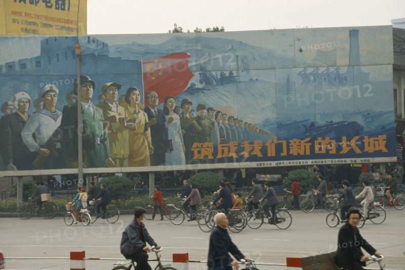 CHINA, Sichuan, Chengdu, ‘Building our new Great Wall’ poster on hoarding beside road with cyclists passing.