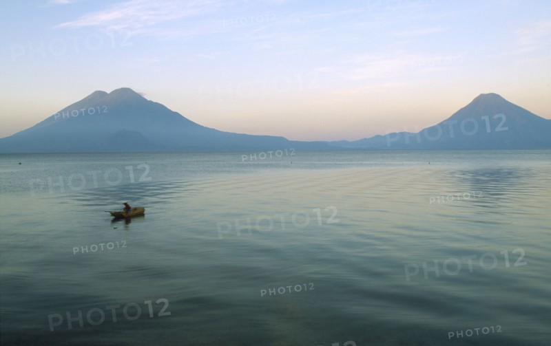 GUATEMALA, Panajachel, Lake Atitlan, View of a boat sailing on the lake with two Volcanoe peaks in the distance.