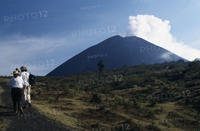 GUATEMALA, Pacaya Volcano, Smoking cone of volcano with people walking a dirt path in the foreground.