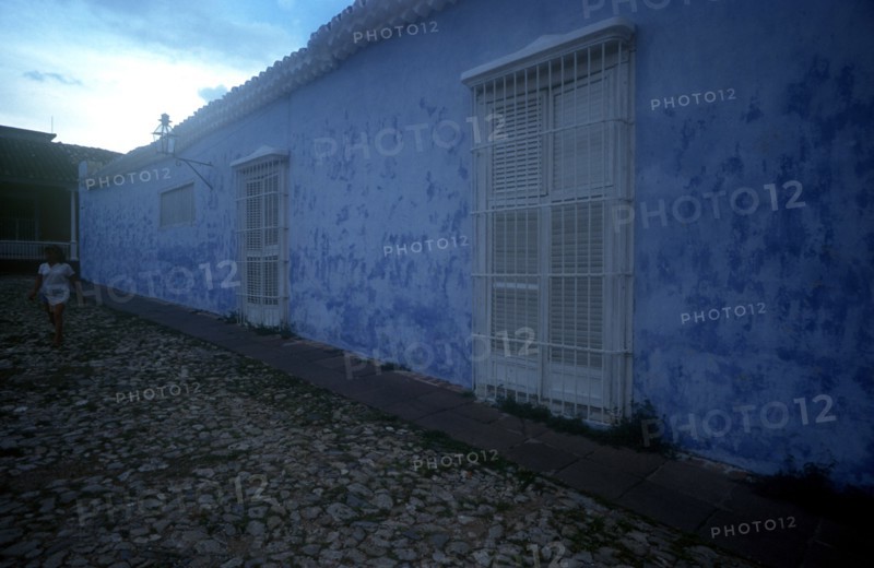 CUBA, Sancti Spiritus, Trinidad, House with blue walls in cobbled street with a woman in white walking past