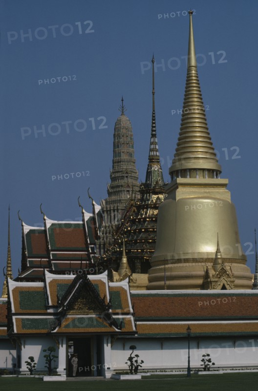 THAILAND, Bangkok, Grand Palace, Aka Wat Phra Kaeo. Exterior view of golden spires and man on guard at the entrance