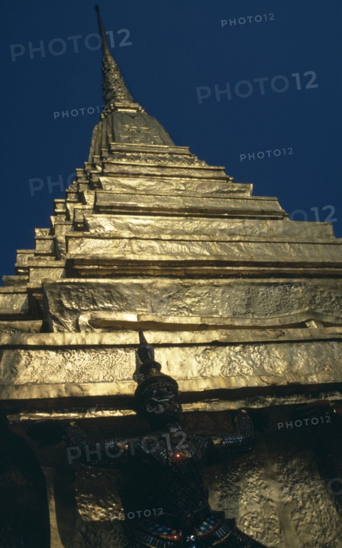 THAILAND, Bangkok, Grand Palace, Wat Phra Kaew. Looking up to detail of statue standing under golden spire