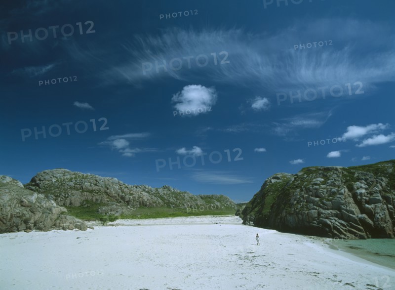 SCOTLAND, Strathclyde, Isle of Mull, White Sand Beach with large moss covered bolders and a woman standing in the distance