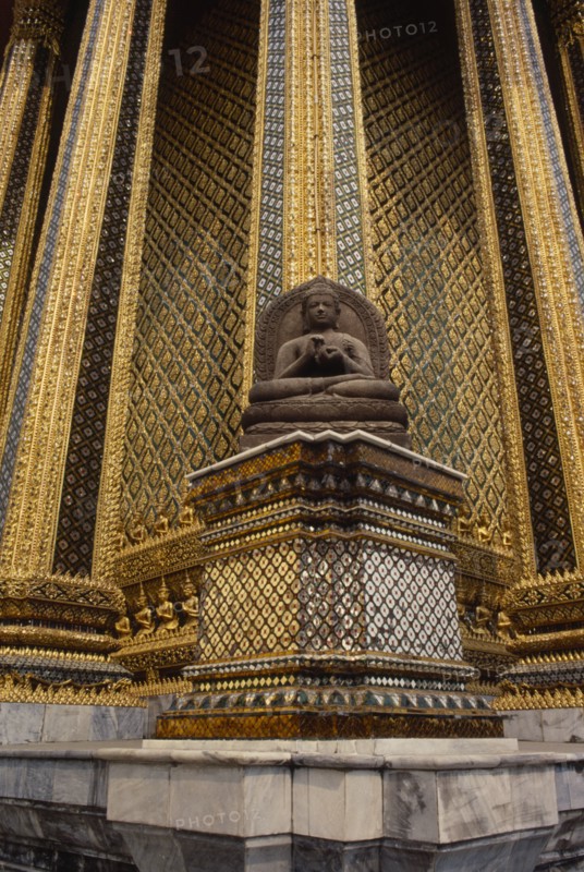 THAILAND, Bangkok, Wat Phra Kaew, Or Grand Palace. Seated buddha statue sitting against golden exterior wall