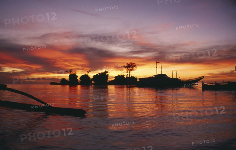 PHILIPPINES, Boracay Island, Rocky outcrops and moored boats silhouetted against pink and orange sunset sky reflected in the water