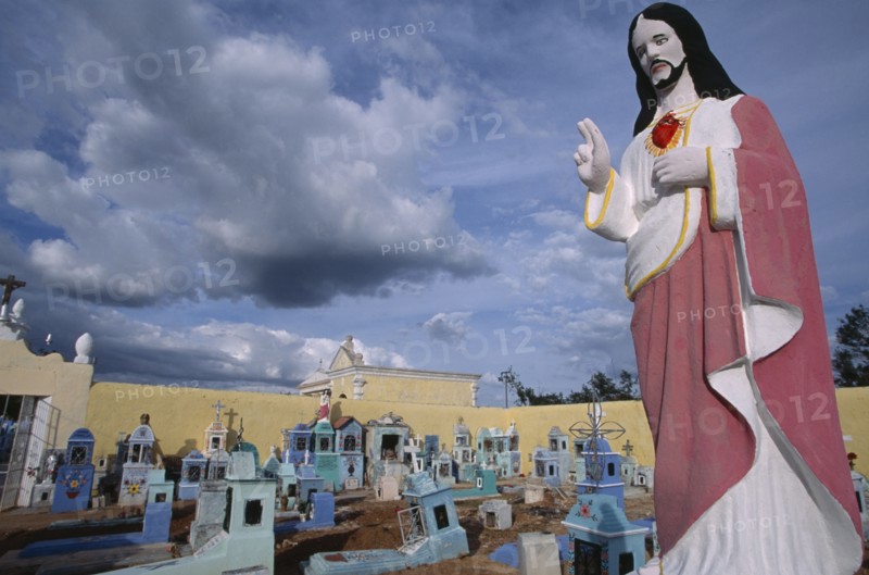 MEXICO, Yucatan, Hoctun, Cemetery with painted religious statue in the foreground and graves painted blue and turquoise behind.