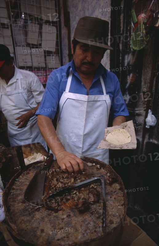 MEXICO, Mexico City, "Man making tacos and enchiladas, chopping meat with a cleaver on a circular block."
