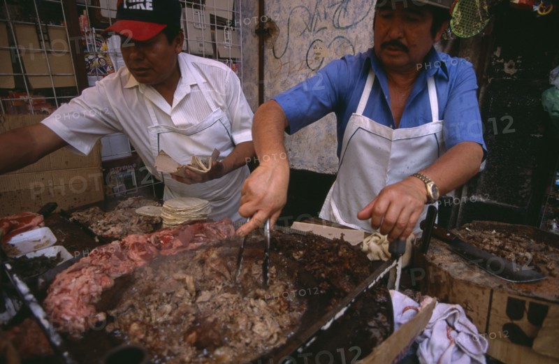 MEXICO, Mexico City, Men cooking meat for tacos and enchiladas on circular hot plate at roadside stall.