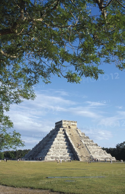 MEXICO, Yucatan, Chichen Itza, "El Castillo, angled view of facade partly framed by tree branches with visitors climbing steep steps to the top."
