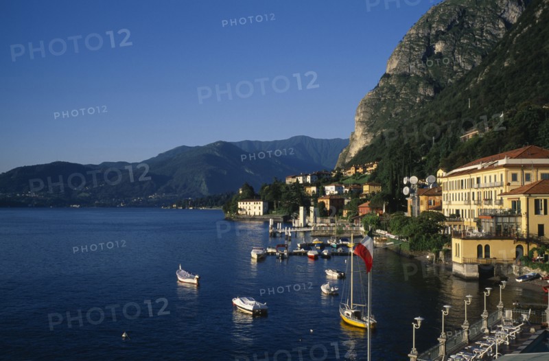 ITALY, Lombardy, Lake Como, Waterfront buildings overlooking moored boats with mountain landscape behind.
