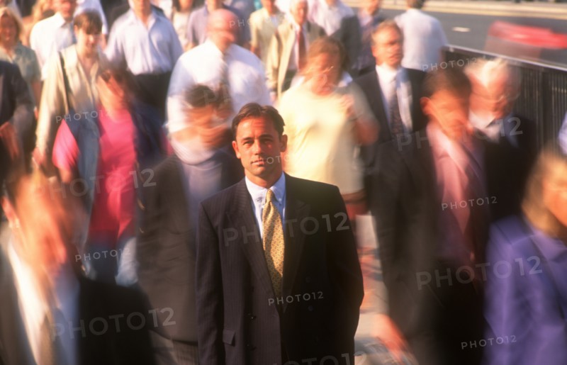 BUSINESS, Commuters, City businessman in suit standing motionless surrounded by crowds in blurred movement.