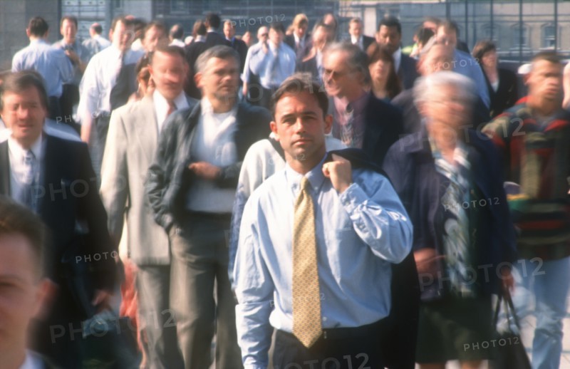 BUSINESS, Commuters, City businessman in shirt and tie holding suit jacket over his shoulder standing motionless surrounded by crowds in blurred movement.