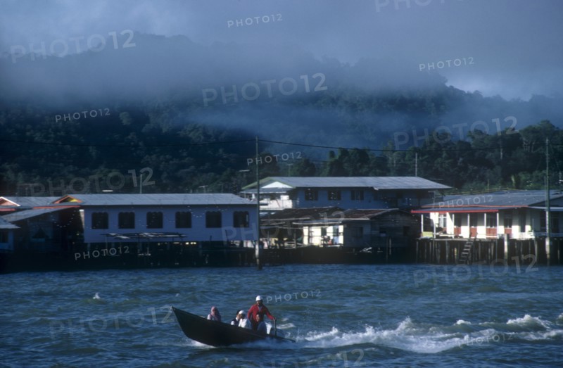 BRUNEI, Bandar Seri Begawan, Morning mist rising from the jungle behind the kampong stilt house village with a water taxi on the river in the foreground