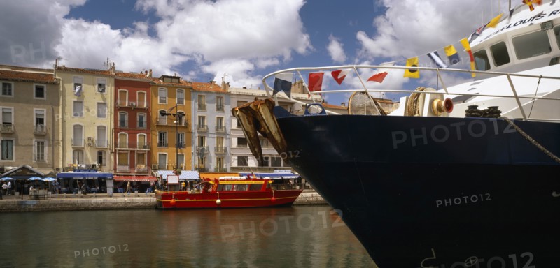 FRANCE, Languedoc-Roussillon, Herault, Sete.  Part view of harbour and colourful waterside buildings with prow of boat draped with flags in the foreground.