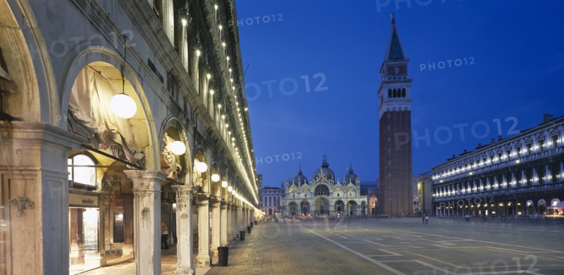 ITALY, Veneto, Venice, Piazza San Marco.  View along the colonnaded Procuratie Vecchie towards the Basilica di San Marco and the Campanile illuminated at dusk.