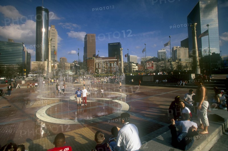 USA, Georgia, Atlanta, "Centennial Olympic Park.  Visitors around paved area with fountains, city skyline behind."