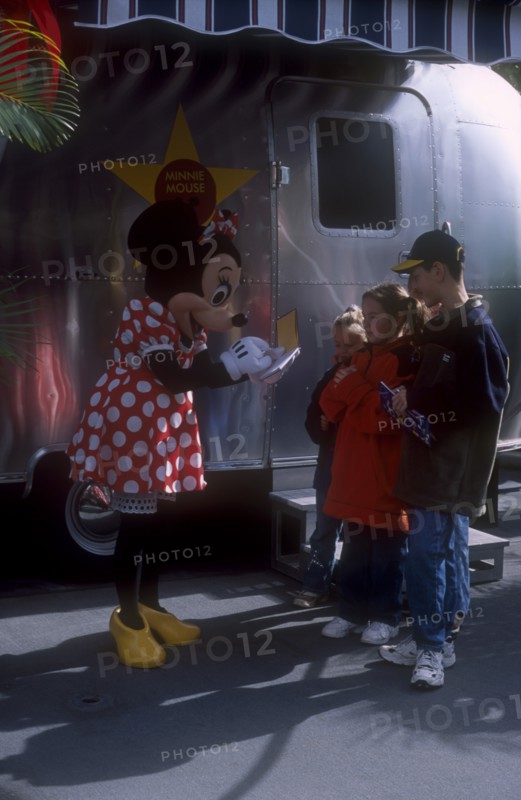 USA, Florida, Orlando, Walt Disney World. Minnie Mouse signing autographs for three children outside her star trailer.