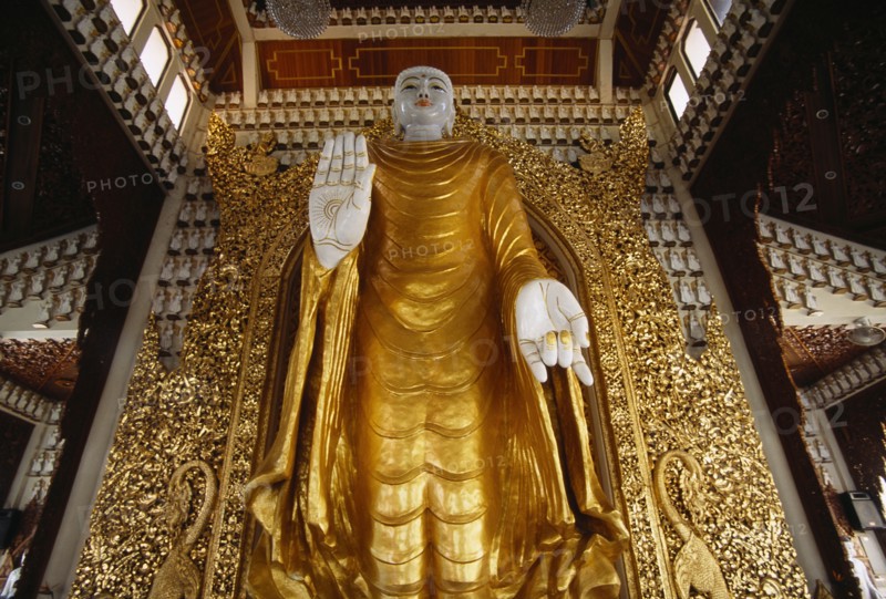 MALAYSIA, Penang, Georgetown, Dharmikarama Burmese Temple.  Interior with large standing Buddha figure with raised hand in gold painted robe and ornate carved gold panel behind.