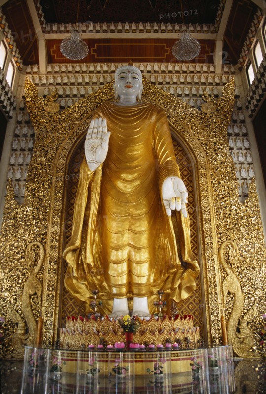 MALAYSIA, Penang, Georgetown, Dharmikarama Burmese Temple.  Interior with large standing Buddha figure with raised hand in gold painted robe and ornate carved gold panel behind.
