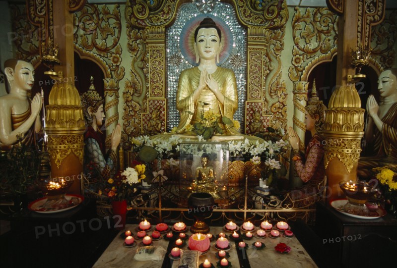 MALAYSIA, Penang, Georgetown, Dharmikarama Burmese Temple.  Interior with pink lotus flower shaped lighted candles in front of large seated Buddha and small golden Buddha figures.
