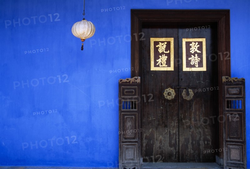 MALAYSIA, Penang, Georgetown, Cheong Fatt Tze Mansion.  Restored Chinese merchants house.  Wooden doorway with gold Chinese letters set into blue painted wall with lantern hanging at side.