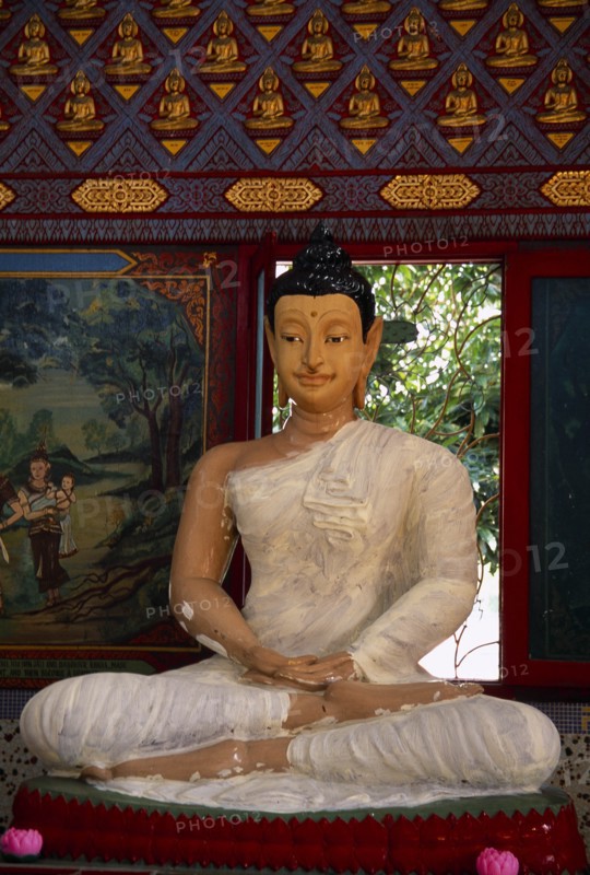 MALAYSIA, Penang, Georgetown, Wat Chayamangkalaram.  Interior with seated Buddha figure in meditative pose framed by red window frame.  Wall painting depicting religious scene at side.