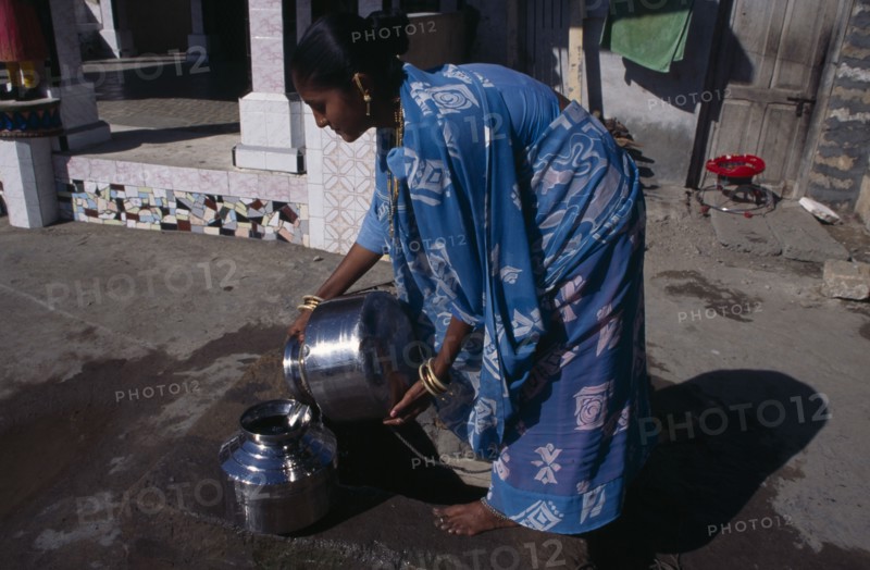 INDIA, Gujurat, Diu , "Young woman wearing blue, printed sari fetching water from well in street."