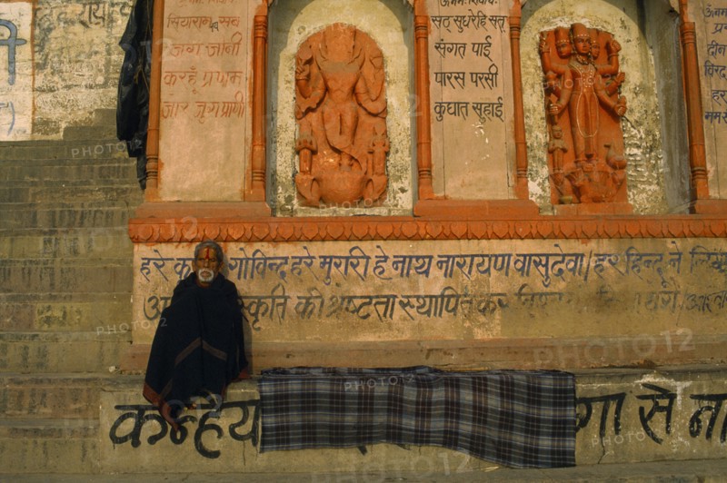INDIA, Uttar Pradesh, Varanasi, Pilgrim sitting near religious wall carvings