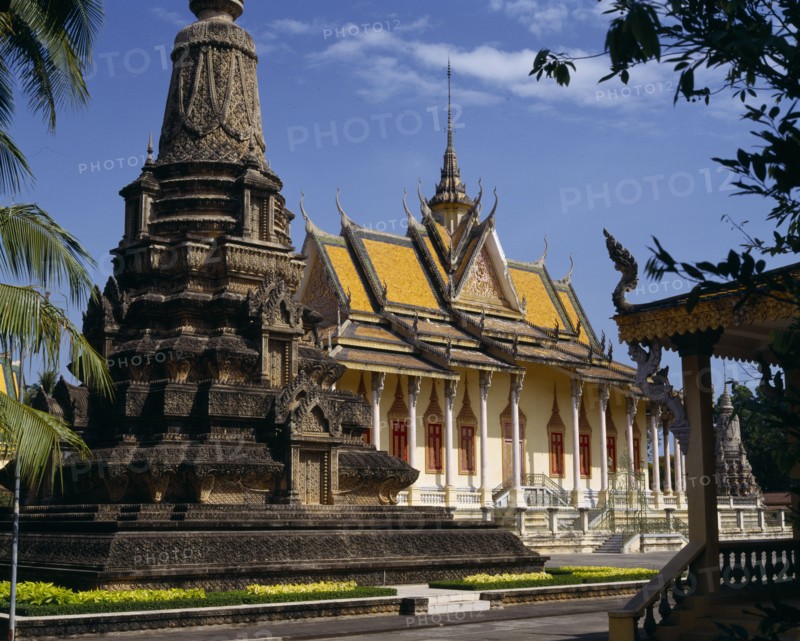 CAMBODIA, Phnom Penh, Silver Pagoda.  Exterior with ornate golden roof with spire and stone monument in foreground.