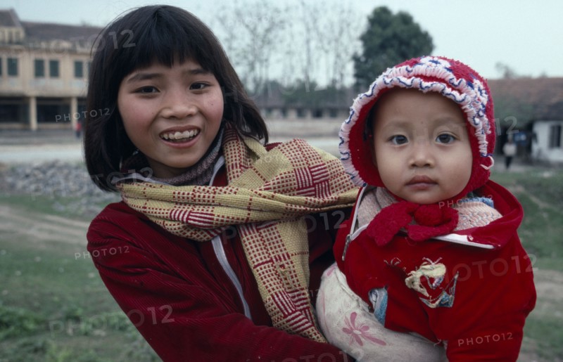 10137264 VIETNAM People Children Portrait of girl holding baby dressed  in red jacket and bonnet