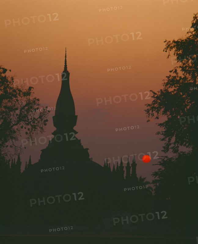 LAOS, Vientiane, Pha That Luang Sacred Stupa silhouetted against red setting sun and orange sky.