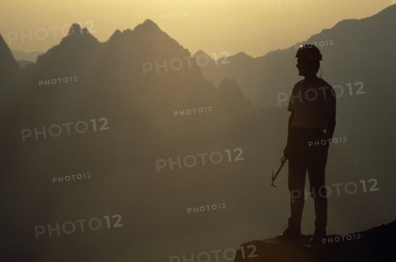 10001972 SPORT Mountineering Climbing Climber in safety helmet standing in partial silhouette against mountain peaks in early morning light. France  Chamonix  Alps.