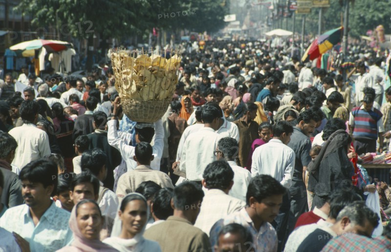 INDIA, General, Crowded street scene with man in centre carrying basket of bread on his head.