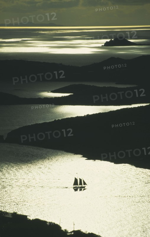 WEST INDIES, US Virgin Islands, St Thomas, Silhouette of two masted sailing ship with three sails up amongst the bays of the coastline