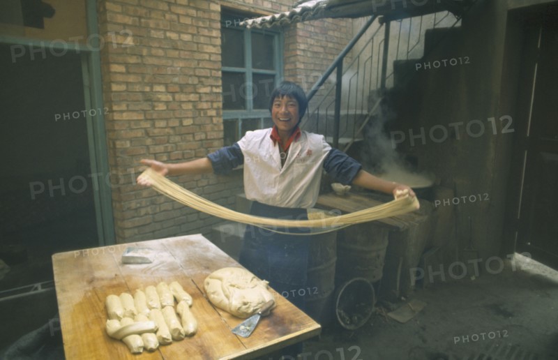 CHINA, Gansu Province, Lanzhou, "Smiling young man making noodles, holding long ribbons of dough in outstretched arms."
