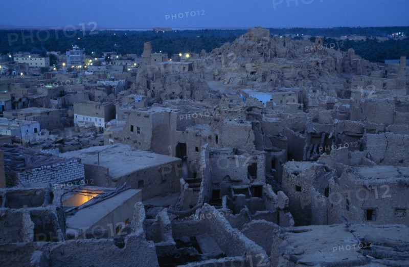 EGYPT, Western Desert, Siwa Oasis, View across town towards Shali Fortress at night with oasis in the background