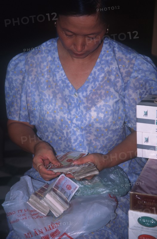 VIETNAM, Hanoi, Seated woman counting out bank notes.