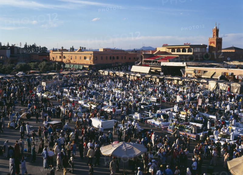 MOROCCO, Marrakech, "Djemma El Fina. Elevated view over busy market square, crowds of people around stalls with buildings behind."