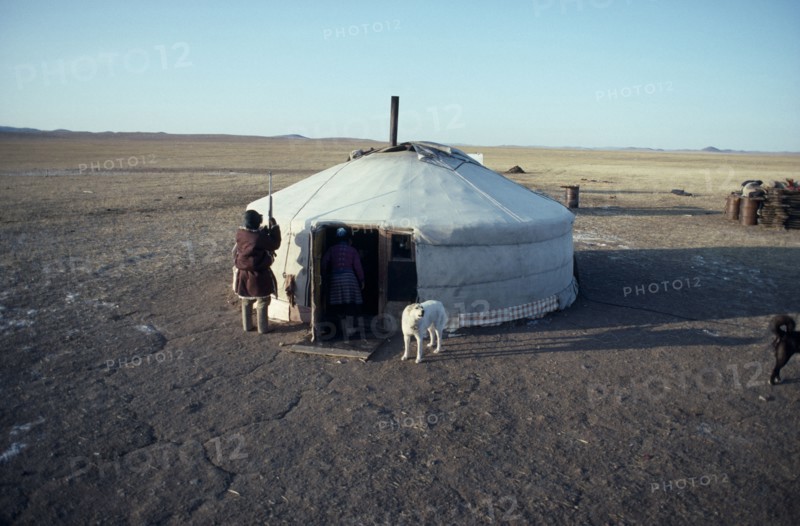 MONGOLIA, People, Ger or yurt in winter camp with dogs tied up outside and herdsman standing beside entrance.