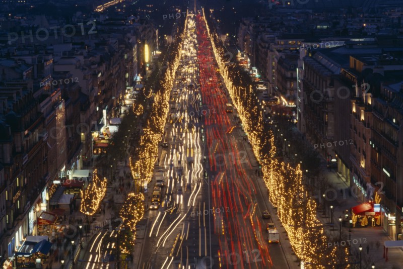 FRANCE, Ile de France, Paris, Les Champs Elysees at night with illuminated shop fronts and traffic light trails.