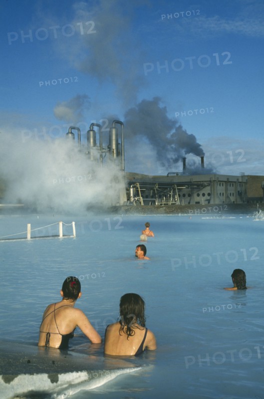 ICELAND, Gullbringu, Reykjanes Peninsula, Blue Lagoon at Svartsengi geo thermal power station. Bathers in the steaming blue water with power plant beyond.