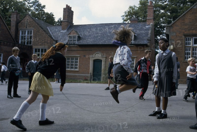 ENGLAND, Birmingham, Primary schoolchildren playing skipping games in playground.