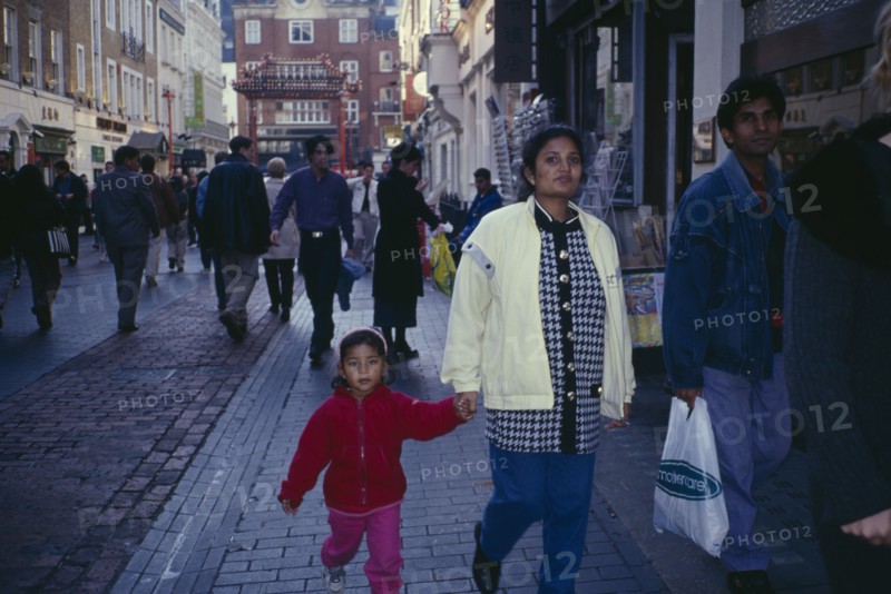 ENGLAND, London, Chinatown.  Mixed crowd of shoppers with young family in foreground.