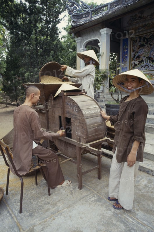 VIETNAM, Hue, Monks husking rice in a traditional hand driven machine