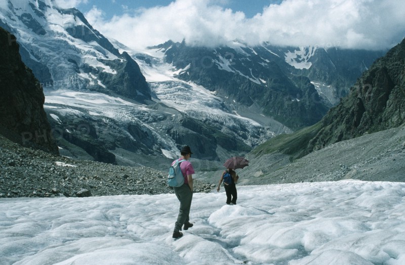 RUSSIA, Caucasus Mountains, Adyr Su Valley, Hikers walking down glacier wearing sun glasses and carrying umbrella to protect against sun.